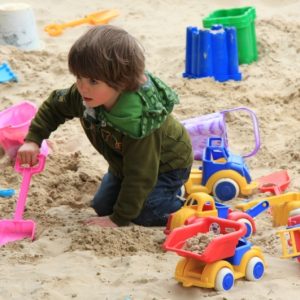 A boy playing with the buckets and spades in the sand pit